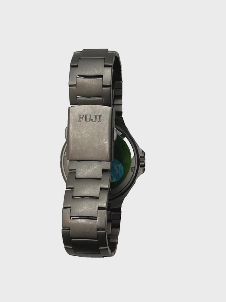 May include: A dark grey FUJI wristwatch with a metal strap. The watch face is visible, showing a green and blue design. The strap is made of interlocking metal links.