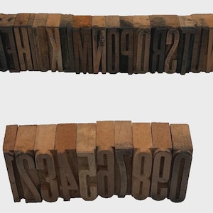 May include: A collection of vintage wooden letterpress blocks arranged in two rows. The top row features the alphabet from A to Z in reverse, while the bottom row displays the numbers 0 through 9 in reverse, all crafted from natural light brown wood.
