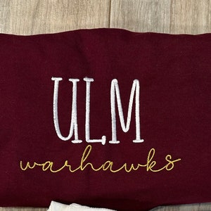 May include: A maroon sweatshirt with the white embroidered letters "ULM" above the gold embroidered word "warhawks". The sweatshirt is made of a soft material and is likely for casual wear.