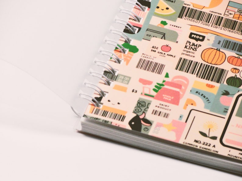 May include: A spiral-bound notebook with colorful, illustrated pages. The pages feature various food-themed graphics, including carrots, pumpkins, and dairy products, along with text such as "Gala Apple" and "Organic Produce."