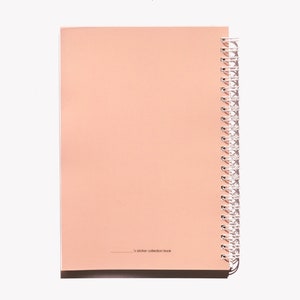 May include: A peach-colored spiral-bound notebook with a white spiral binding. The notebook is open, revealing blank pages. The text "s sticker collection book" is printed at the bottom of the page.