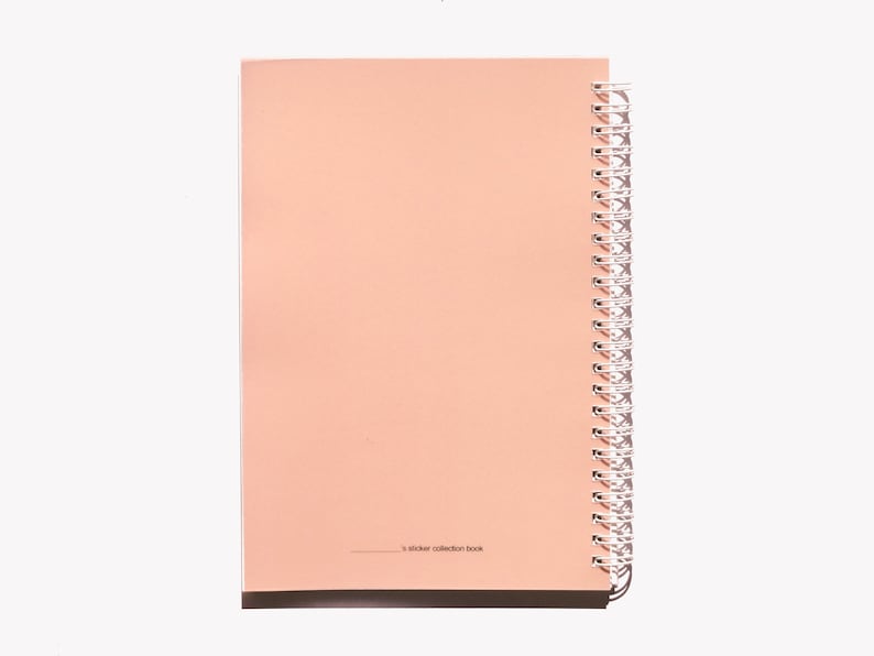 May include: A peach-colored spiral-bound notebook with a white spiral binding. The notebook is open, revealing blank pages. The text "s sticker collection book" is printed at the bottom of the page.