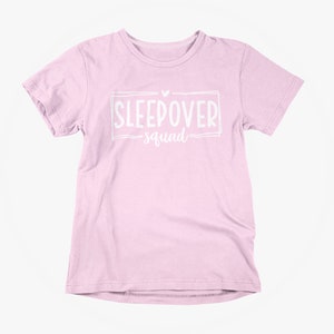 May include: A pink t-shirt with a white graphic that says "Sleepover Squad" with a heart above the text.