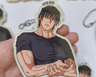 May include: A black and white anime-style keychain featuring a man with short black hair and a black t-shirt. He is holding his hands together in front of him.