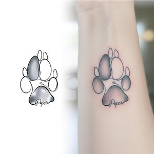Dog paw print line art tattoo on wrist next to a realistic ink shading. Meaningful pet memorial tattoo design from photo.