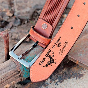 May include: A brown leather belt with a silver buckle. The belt has a rooster design and the text "I love your & I love you Elizabeth" engraved on it.