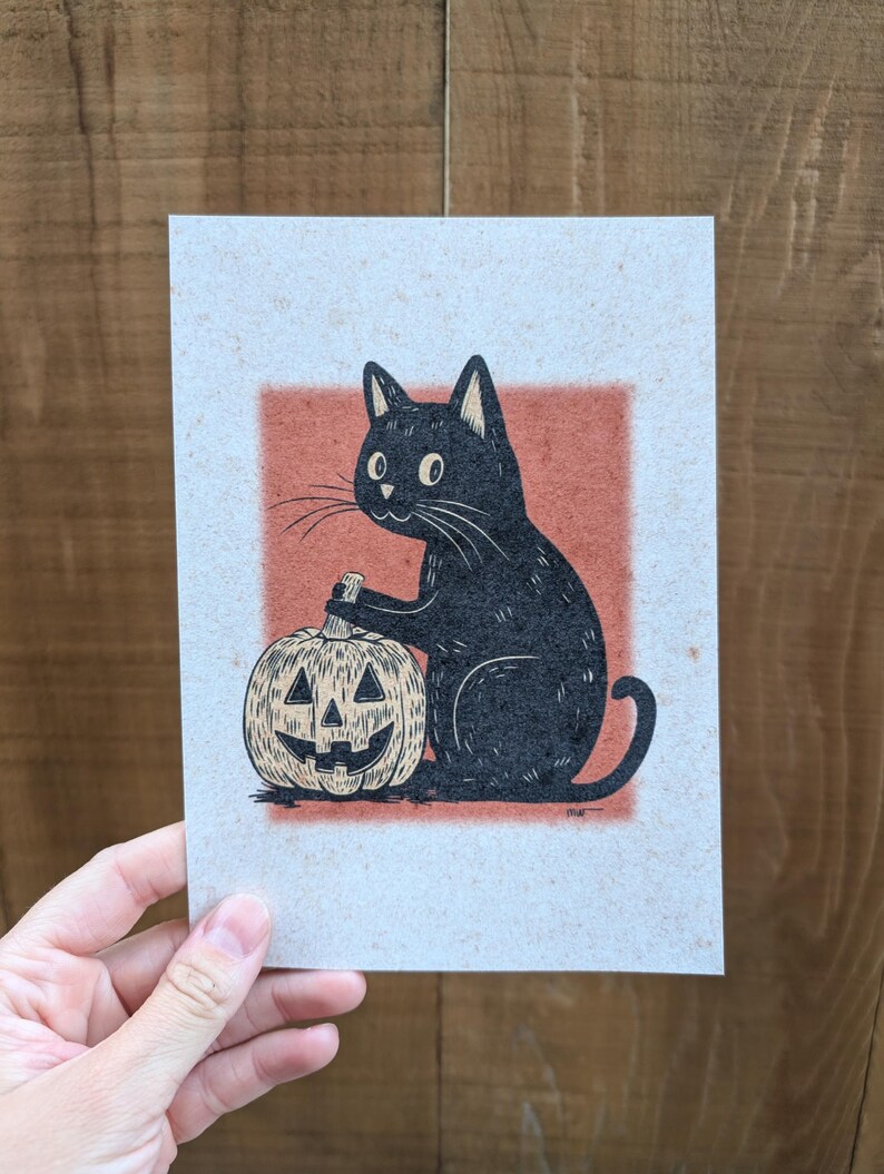 May include: A black cat illustration with a carved pumpkin. The cat is seated, holding a carving tool, with the pumpkin in front. The artwork is on textured paper with a red-orange square background, perfect for Halloween.