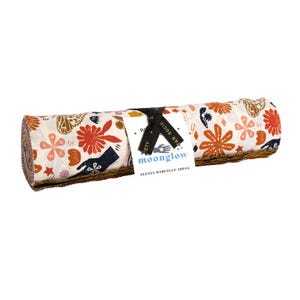 May include: A rolled bundle of fabric strips featuring a cream background with a repeating pattern of orange flowers, dark blue hands, and butterflies. A black ribbon secures the roll with a white tag printed with the text Moonglow Alexia Marcelle Abegg.