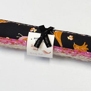 May include: A stack of fabric squares featuring a black background with orange birds and pink flowers. The fabric squares are bundled together with a black ribbon and a label that reads "Ruby Star Society Birdie Word by  Kimberly Kight".