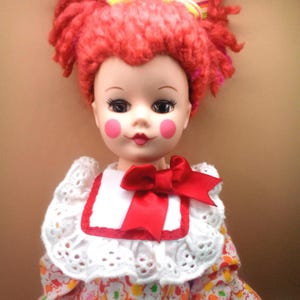 May include: A white ceramic mug with a black handle and the text "But First, Coffee" in a bold, black font. The mug is set against a blurred background, suggesting a cozy setting.