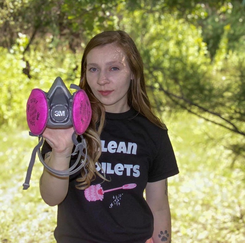 May include: A gray 3M respirator mask with two circular pink filters attached to the sides. The mask features a central circular valve and adjustable gray straps. The filters are clearly labeled with the text 2097 and the 3M brand logo.