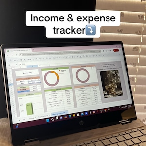May include: A laptop displaying an income and expense tracker spreadsheet. The screen shows a monthly overview with income and expense categories, charts, and financial data. The text "Income & expense tracker" is at the top of the image.