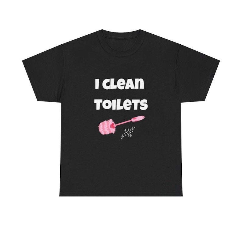 May include: A black short-sleeve t-shirt featuring the white text "I CLEAN TOILETS" printed on the chest. Below the text is a graphic of a pink toilet brush with a fluffy head and a small white sparkle icon to the right of the brush handle.