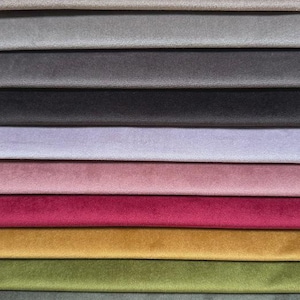 Könnte beinhalten: Eine Sammlung gestapelter Stoffmuster mit einer glatten, samtartigen Textur. Die Farben umfassen Weiß, Beige, Grau, Anthrazit, Lavendel, Altrosa, Magenta, Senfgelb, Olivgrün, Salbei, Petrol und leuchtendes Blau.