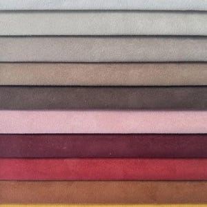 May include: A fabric swatch sample book featuring a vertical arrangement of suede-like material strips in various colours including light grey, beige, taupe, dark brown, soft pink, deep burgundy, bright red, rust orange, mustard yellow, and dark teal.