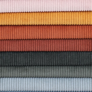 May include: A stack of corduroy fabric swatches in various colors, including white, brown, pink, yellow, orange, red, gray, blue, and black.