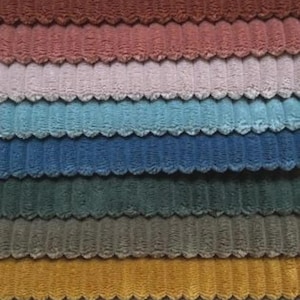 May include: A collection of stacked fabric swatches featuring a distinct corduroy texture with raised vertical ridges. The color palette includes shades of beige, brown, terracotta, pink, light blue, navy, dark green, olive, mustard, white, and gray.