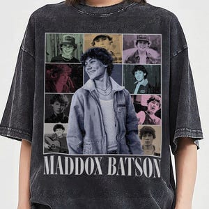 May include: A charcoal black acid-wash t-shirt featuring a large graphic print of Maddox Batson. The design includes a central portrait surrounded by eight smaller images of the same individual in various settings, with the name MADDOX BATSON printed in large white capital letters at the bottom.