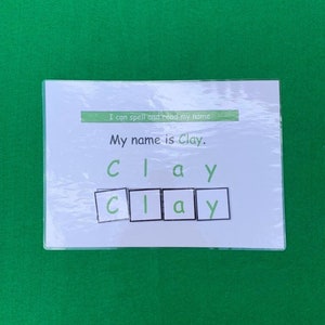 May include: A white card with the text "I can spell and read my name. My name is Clay." and the word "Clay" spelled out with letter tiles.