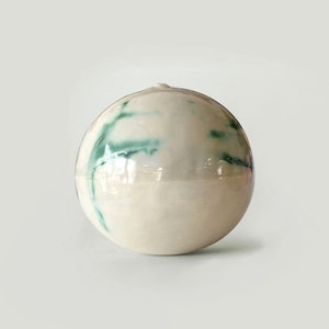 May include: A white ceramic sphere with green streaks of glaze.