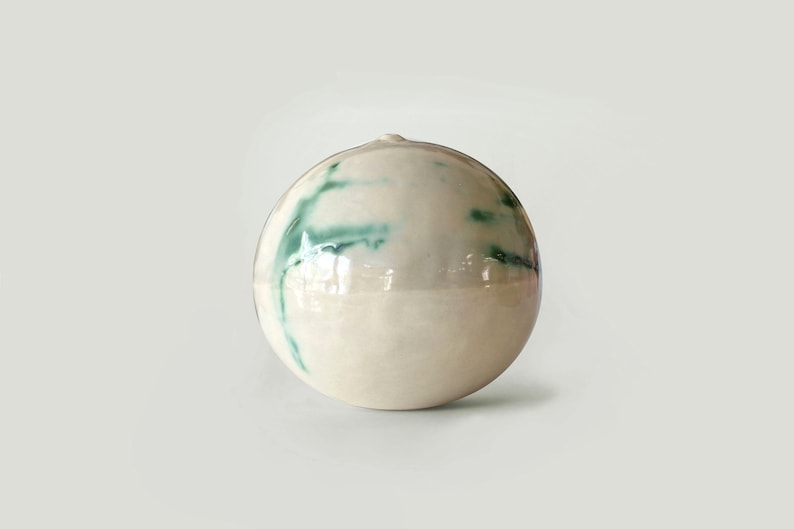 May include: A white ceramic sphere with green streaks of glaze.