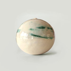 May include: A white ceramic vase with a round shape and green streaks of glaze.