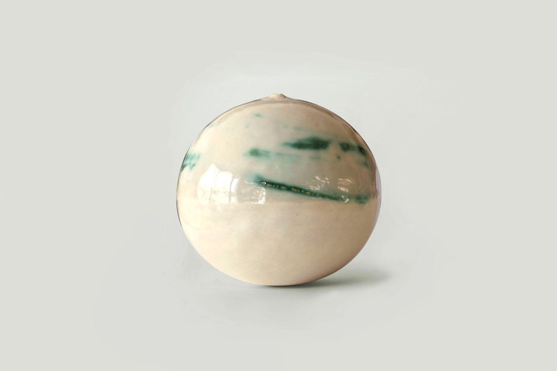 May include: A white ceramic vase with a round shape and green streaks of glaze.