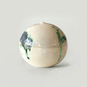 May include: A white ceramic sphere with green and blue abstract designs. The sphere is smooth and glossy.