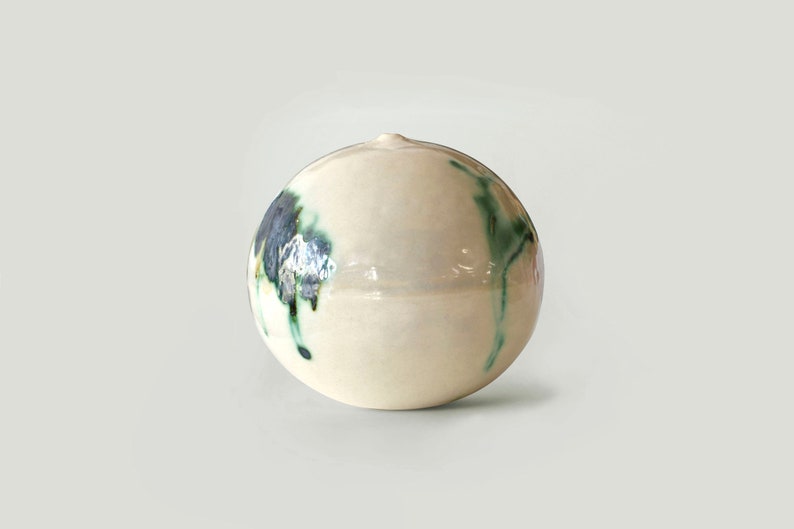 May include: A white ceramic sphere with green and blue abstract designs. The sphere is smooth and glossy.