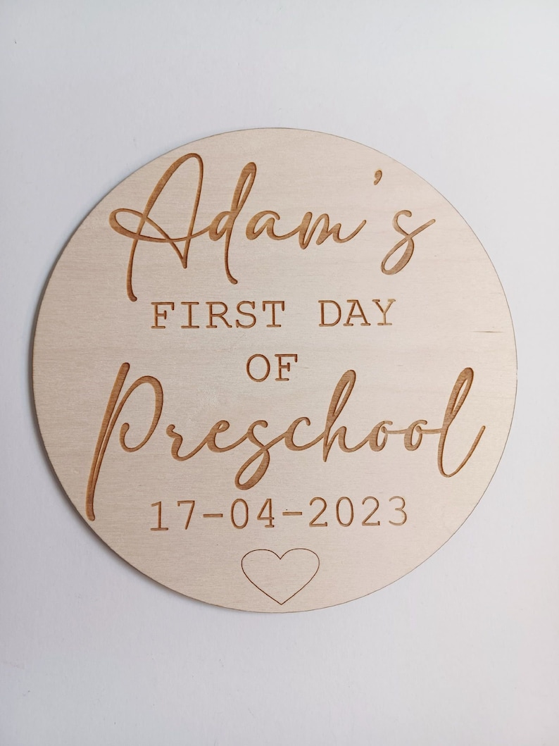 May include: A round wooden sign with the text "Adam's First Day of Preschool 17-04-2023" and a small heart.