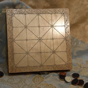 May include: A wooden board game with a decorative border and etched grid pattern. The board is light brown, and several game pieces are scattered around it. The game pieces are small, round, and have a dark brown and white color scheme.