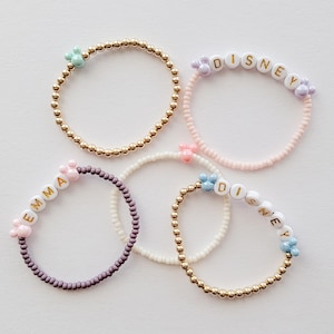 May include: Four beaded bracelets with different colored beads and charms. The bracelets spell out the names "Emma", "Disney", and "Disney".