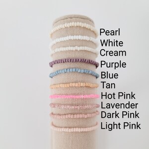 May include: A display of ten beaded bracelets in various colors, including pearl, white, cream, purple, blue, tan, hot pink, lavender, dark pink, and light pink.