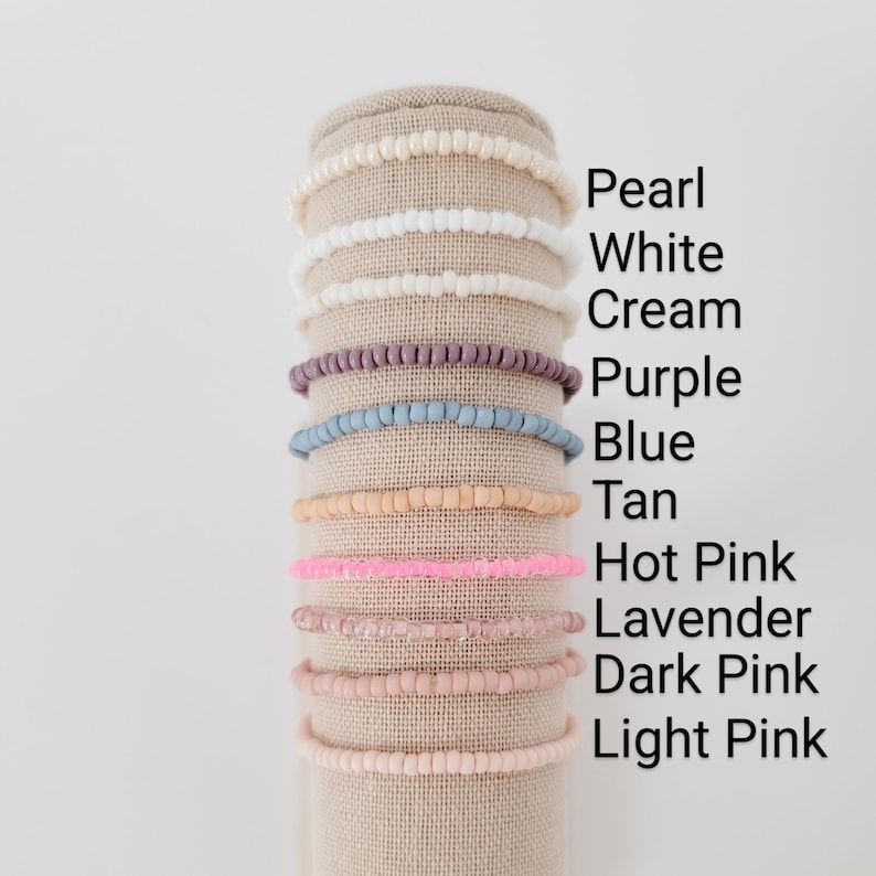 May include: A display of ten beaded bracelets in various colors, including pearl, white, cream, purple, blue, tan, hot pink, lavender, dark pink, and light pink.