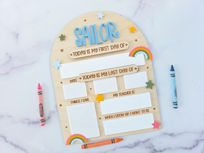 May include: Wooden first day of school sign with the name "SAILOR" in blue letters. The sign includes spaces for "Today is my first day of" and "Today is my last day of". Colorful crayons and star accents are included.