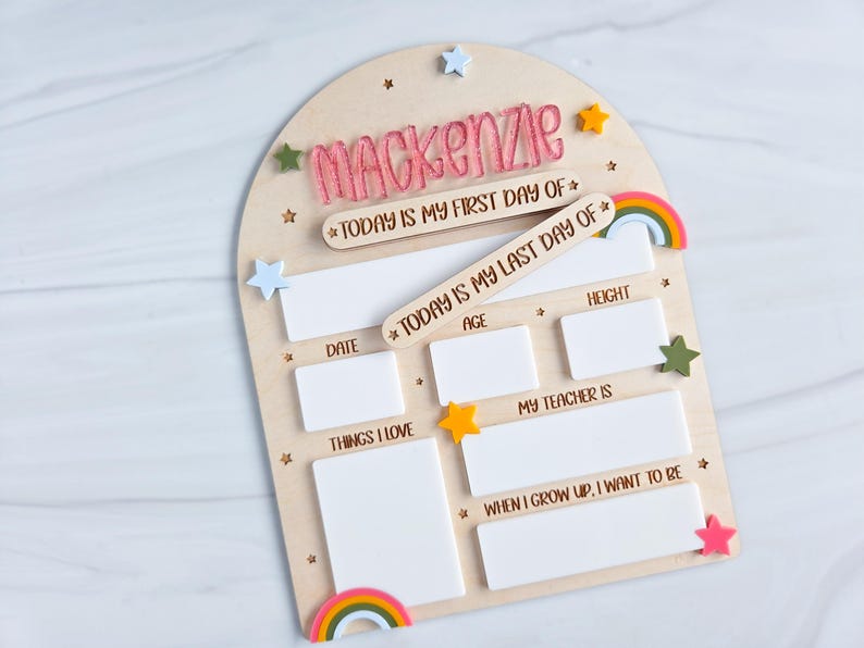 May include: Wooden first and last day of school board with the name "Mackenzie" in pink. Includes spaces for date, age, height, things I love, teacher, and future aspirations. Decorated with stars and rainbows.