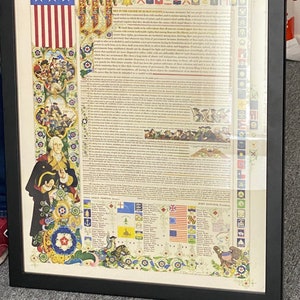 May include: A framed print of the Declaration of Independence, a historical document signed by the founding fathers of the United States of America. The document is surrounded by decorative floral borders and includes a depiction of the American flag.