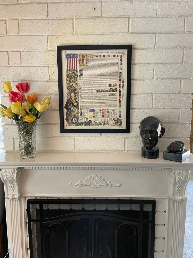 May include: A framed print of the Declaration of Independence with a decorative border. The print is hanging on a white brick wall above a white fireplace with a black metal grate.