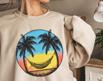 May include: Beige sweatshirt with a circular graphic depicting palm trees, a hammock, and a sunset. The graphic uses blue, yellow, orange, and black. The text "Pretty Trendy Tee" is at the bottom of the image.