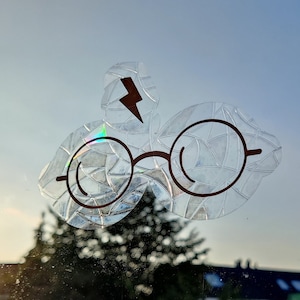 Puede incluir: Una pegatina transparente con un rayo y un par de gafas. Las gafas están delineadas en negro y tienen un diseño texturizado y estampado.