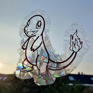 Puede incluir: Una pegatina holográfica con un dibujo en blanco y negro de un personaje de Pokemon con una cola de fuego.