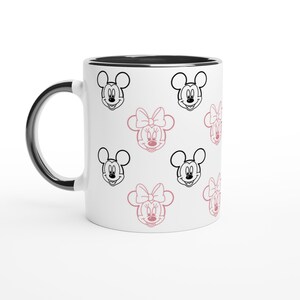 K&ouml;nnte beinhalten: Wei&szlig;er Keramikbecher mit schwarzem Rand und Griff. Der Becher hat ein sich wiederholendes Muster aus schwarzen und rosa Minnie Mouse und Mickey Mouse Gesichtern. Das Design ist verspielt und skurril. Der Becher ist f&uuml;r hei&szlig;e oder kalte Getr&auml;nke geeignet.