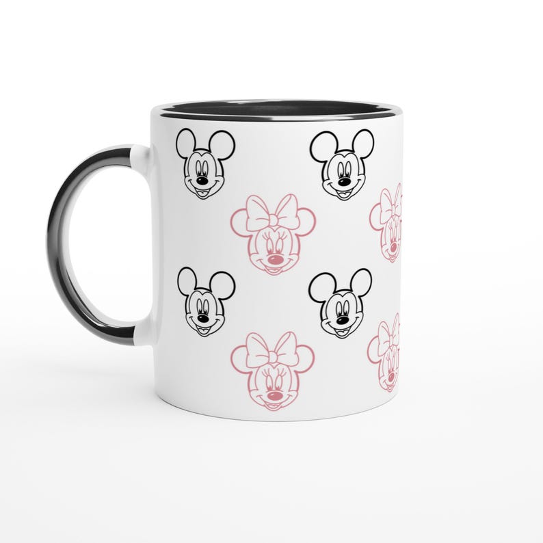 K&ouml;nnte beinhalten: Wei&szlig;er Keramikbecher mit schwarzem Rand und Griff. Der Becher hat ein sich wiederholendes Muster aus schwarzen und rosa Minnie Mouse und Mickey Mouse Gesichtern. Das Design ist verspielt und skurril. Der Becher ist f&uuml;r hei&szlig;e oder kalte Getr&auml;nke geeignet.