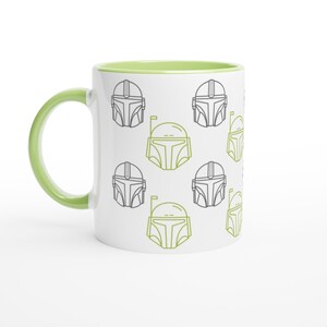Op de afbeelding: Witte keramische mok met een groene handgreep en binnenkant. De mok heeft een herhalend patroon van gestileerde Mandalorian helm ontwerpen in groen en grijs. Een eenvoudig en modern ontwerp voor fans van de serie.