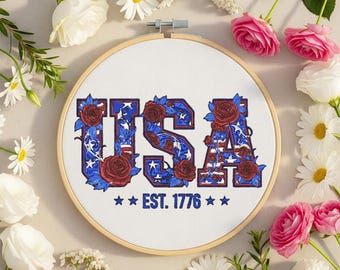 May include: An embroidery hoop with the word "USA" in red, white, and blue, decorated with roses and stars. The text "EST. 1776" is below the word "USA". The words "Embroidery Design" are at the top.