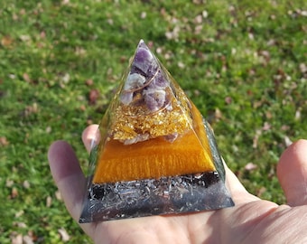 May include: A small pyramid made of clear resin with layers of amethyst, gold flakes, and black crystals. The pyramid is about 2 inches tall and is held in a hand.