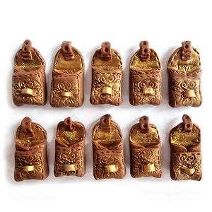 Op de afbeelding: Tien miniatuur bruine leren tassen met gouden accenten en glitter van binnen. De tassen zijn open en hebben een klep sluiting. De tassen zijn gerangschikt in twee rijen van vijf.