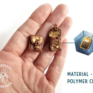 Op de afbeelding: Twee miniatuur bruine leren tassen met gouden accenten en gespen. De tassen zijn gemaakt van polymer clay en worden in een hand getoond. De afbeelding bevat ook een close-up van een van de tassen in een zeshoekig frame.