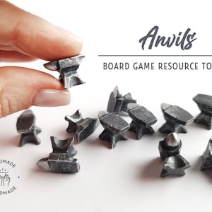 May include: A set of nine silver metal miniature anvils, used as game pieces or tokens. The anvils are handmade and have a rustic, aged look. The text "Anvils Board Game Resource Tokens" is visible in the image.