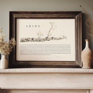 May include: A framed print with the word "ABIDE" in a simple black font. The print features a black and white illustration of a tree branch with the text "I am the true vine, and my Father is the vinedresser. Every branch in me that does not bear fruit he takes away, and every branch that does bear fruit he prunes, that it may bear more fruit." John 15:1-2